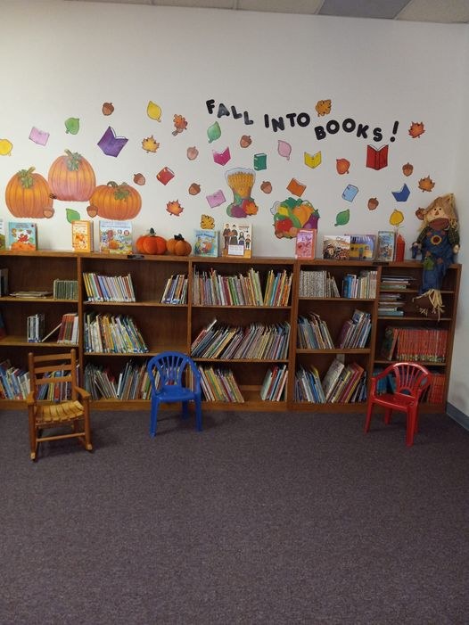 Book, leaves and pumpkins falling display over shelves of books in the children's area.